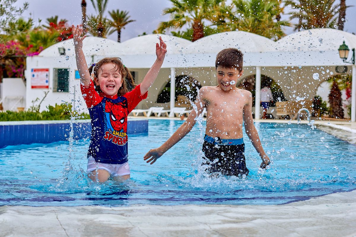Two children playing and splashing in an outdoor swimming pool
