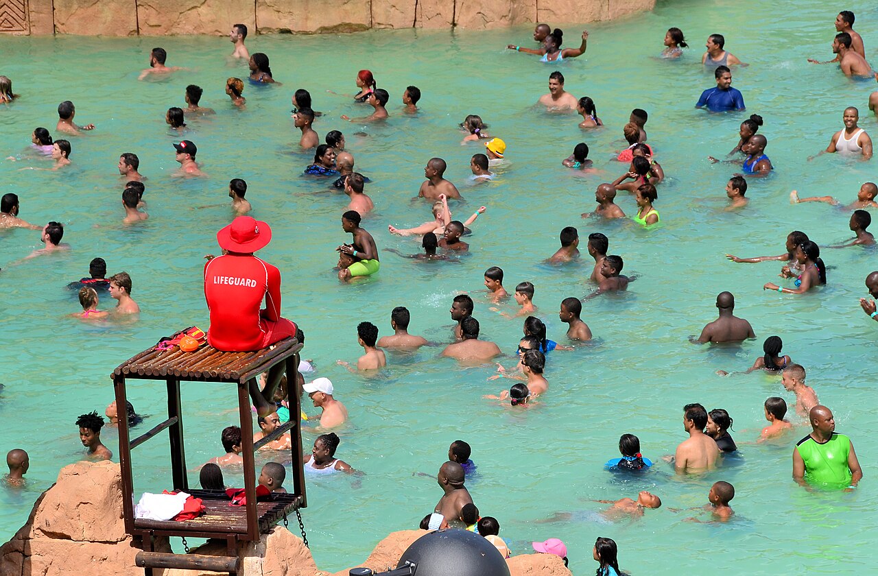 A lifeguard in a red uniform supervising swimmers in a swimming pool